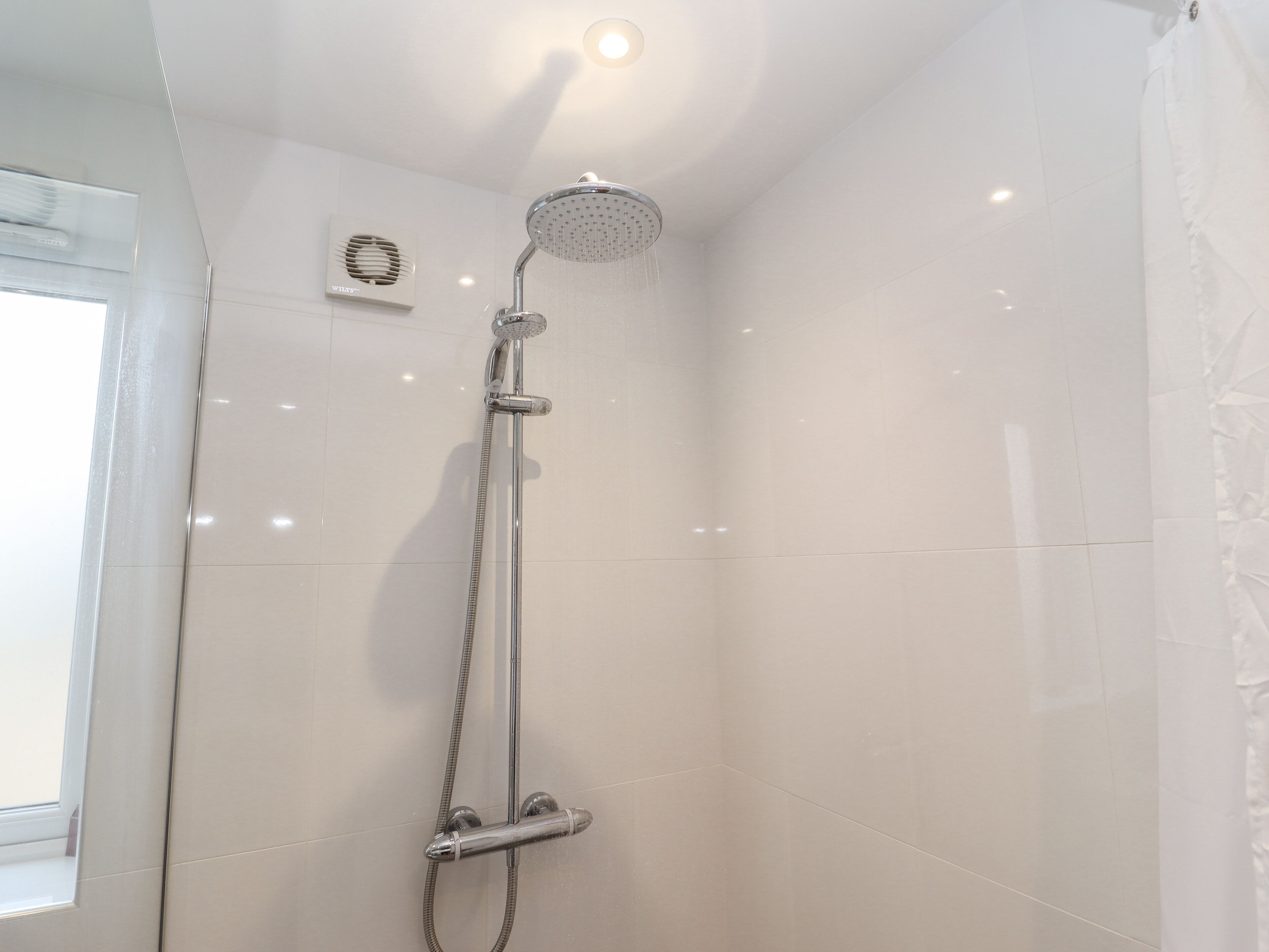 A modern shower with a handheld showerhead, a wall-mounted control panel, and a window for natural light.