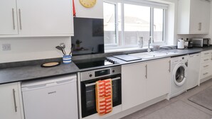 Ett modernt kök med vita skåp, en svart bänkskiva, en inbyggd ugn, en diskmaskin, en tvättmaskin och ett fönster med utsikt över omgivningen.
