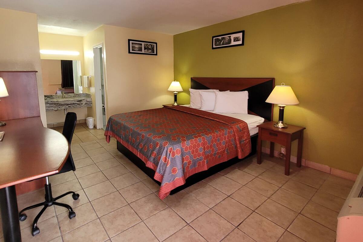 A hotel room with a bed, two bedside lamps, a desk with a chair, and a small table.