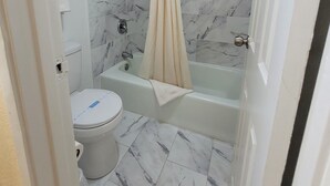 Et badeværelse med toilet, badekar og bruseforhæng.