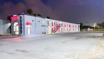 A motel with a red and white facade, a visible entrance, and a staircase leading to the upper floors.