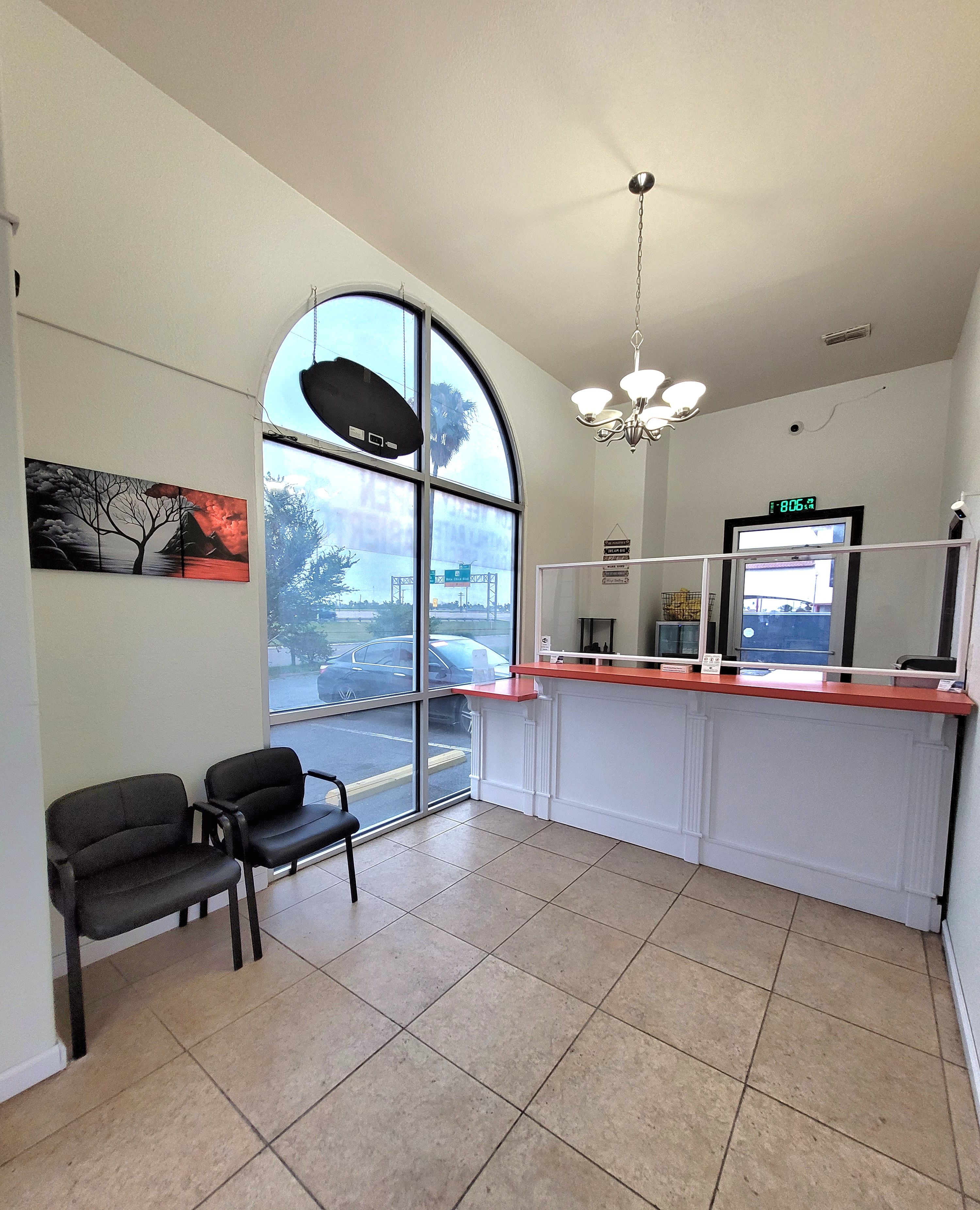 A reception area with a large arched window, two black chairs, a reception desk, and a ceiling light fixture.