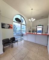 A reception area with a large arched window, two black chairs, a reception desk, and a ceiling light fixture.