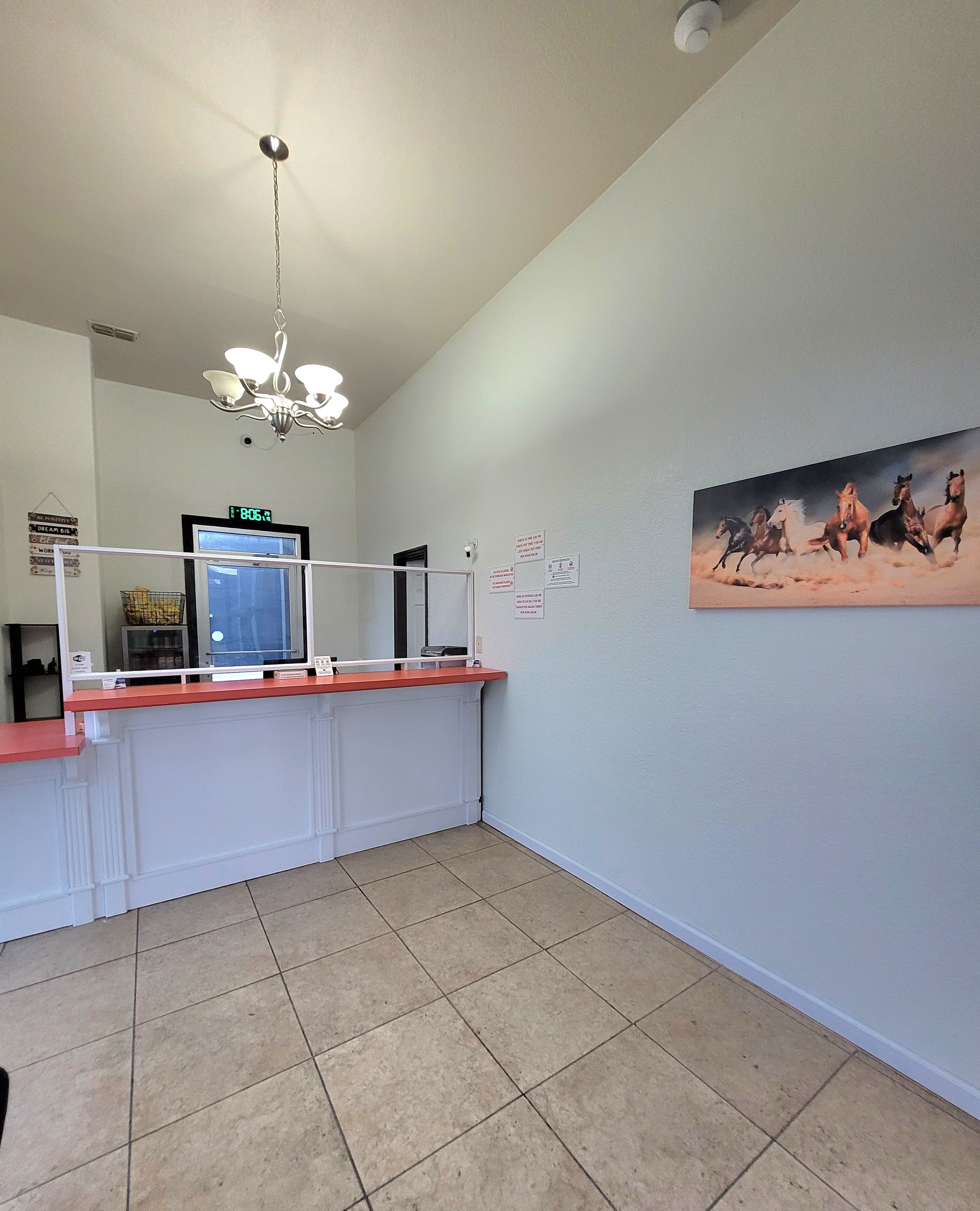 A spacious room with a tiled floor, a reception desk, a digital clock, a chandelier, and a painting of horses on the wall.