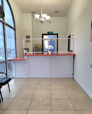 A reception area with a counter, a chandelier, a digital clock, and a view through a large window. - La Vista Motel (Brownsville)