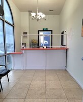 A reception area with a counter, a chandelier, a digital clock, and a view through a large window.
