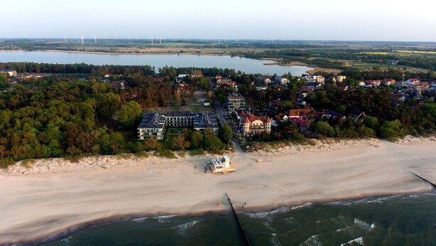 Oversigtsbillede af en kystby med en strand, huse og vindmøller i det fjerne.