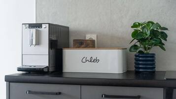 Una cucina con una macchina per il caffè, una pianta in un vaso blu e un mobiletto a cassetti con l'etichetta 'Chleb'.