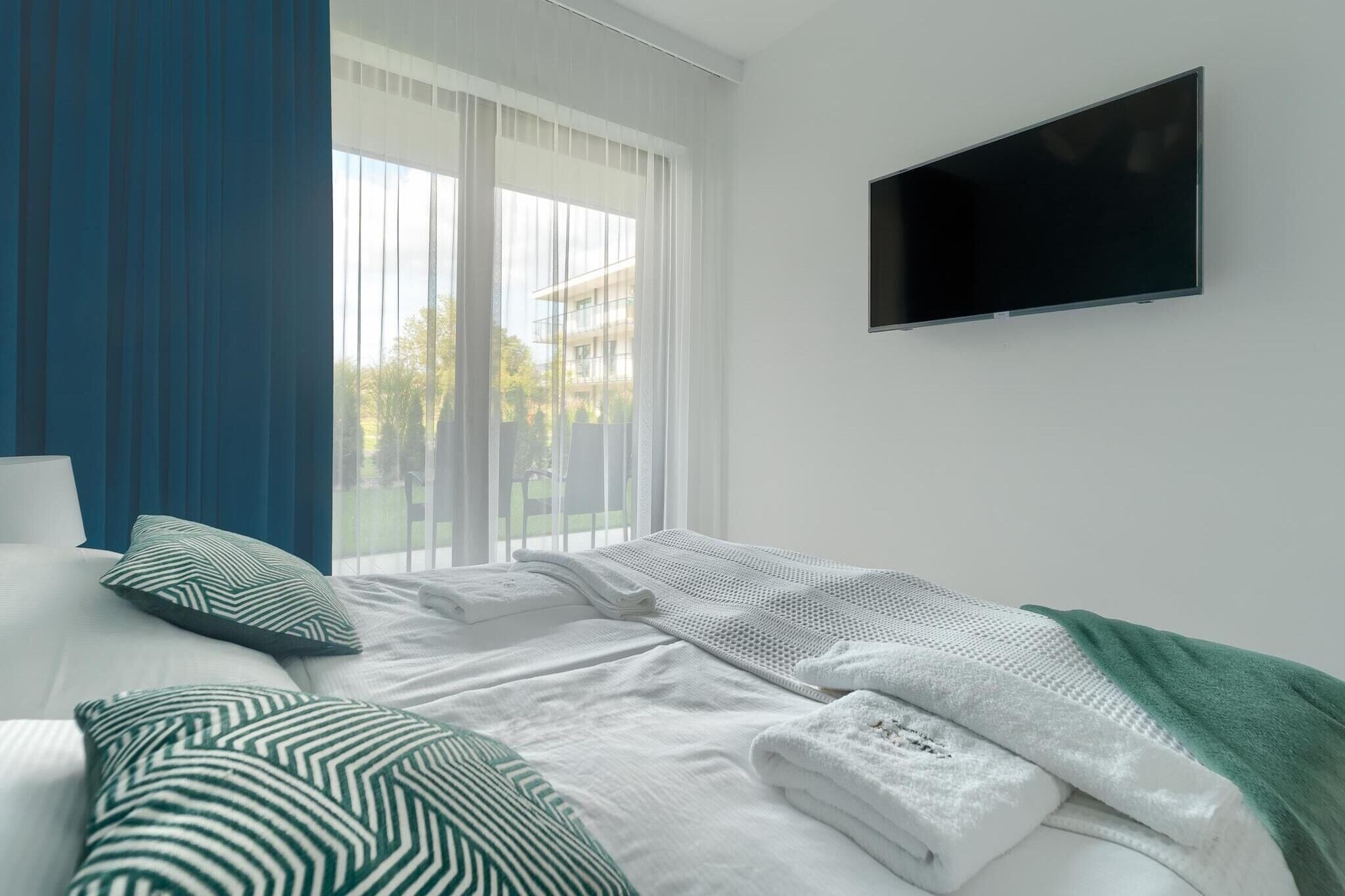 Une chambre d’hôtel moderne avec un grand lit, un téléviseur à écran plat fixé au mur et une vue sur un bâtiment à l’extérieur, visible par la fenêtre.
