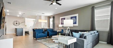 A modern living room with a grey sofa, blue armchairs, a white coffee table, and a ceiling fan.