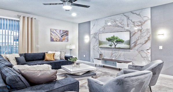 A modern living room with a sectional sofa, a coffee table, and a flat-screen TV mounted on the wall.