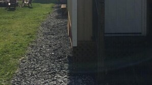 A small wooden cabin with a door, a gravel path leading to it, and a bench in the background. - Cottage with sunset view and much more (Alburgh)