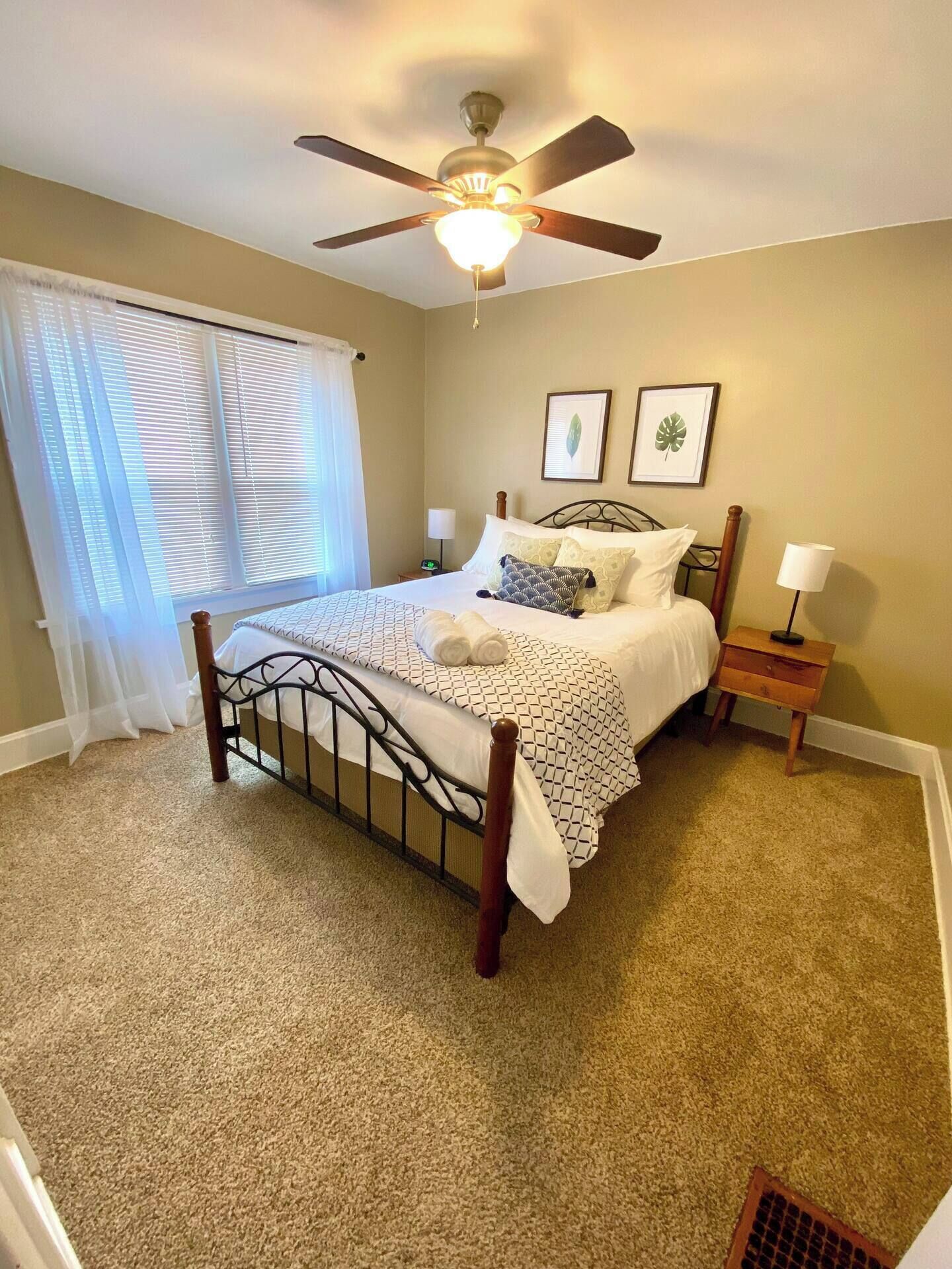 A bedroom with a bed, a ceiling fan, two wall-mounted lamps, and a window with blinds.