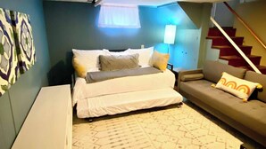 Un dormitorio con cama, sofá, sillón, escalera y pared decorada.