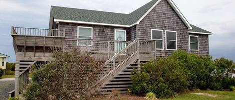 A two-story house with a wooden deck and a staircase leading to the upper floor.