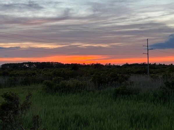 Un coucher de soleil sur un champ d’herbe, avec une ligne électrique et un poteau électrique.