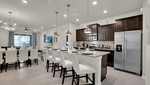 A modern kitchen with dark wood cabinets, stainless steel appliances, and a central island with white bar stools. - Last Minute Disney Getaway! Private Pool, Hot Tub & Game Room. Book Now! #72773 (Orlando)