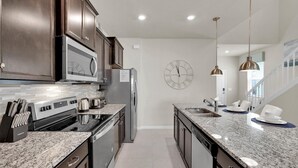A modern kitchen with dark wood cabinets, stainless steel appliances, granite countertops, and a clock on the wall. - Last Minute Disney Getaway! Private Pool, Hot Tub & Game Room. Book Now! #72773 (Orlando)