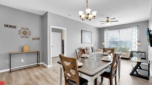 Ein Essbereich mit Holztisch, Stühlen und einer Chandelier. Ein Deckenventilator und ein Fenster mit Vorhängen sind vorhanden.