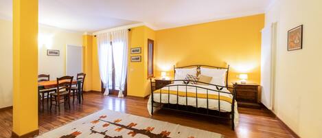 Habitación de hotel con cama, mesitas de noche, escritorio y sillas, y una alfombra estampada.