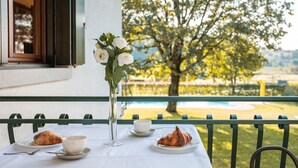 Une table avec des croissants et une tasse de café, un vase rempli de fleurs et une vue sur un arbre et une piscine.