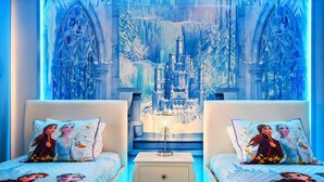Une chambre à coucher avec deux lits, chacun agrémenté d’oreillers assortis et surmontée d’un lustre central.