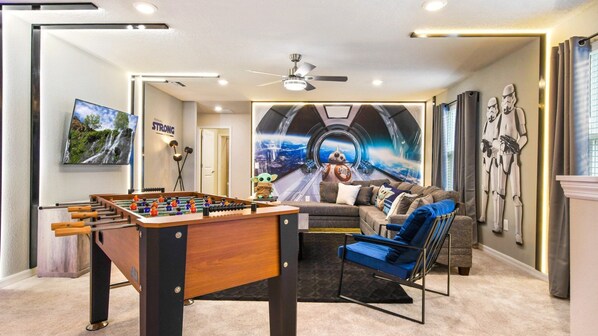 A room with a foosball table, a sofa, a wall with Star Wars-themed artwork, and a ceiling fan. - Last Minute Disney! Private Pool, Hot Tub, Game Room & Themed Bedrooms. Book Now! #79745 (Orlando)