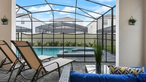 A covered outdoor area with a pool, lounge chairs, and a sofa.
