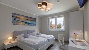 A modern bedroom with a bed, bedside tables, a desk, and a window with a view. - Exclusives Appartement auf Fehmarn (Petersdorf)