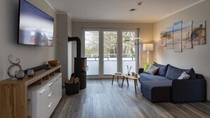 A modern living room with a flat-screen TV, a sofa, a wooden console, and a fireplace. - Exclusives Appartement auf Fehmarn (Petersdorf)