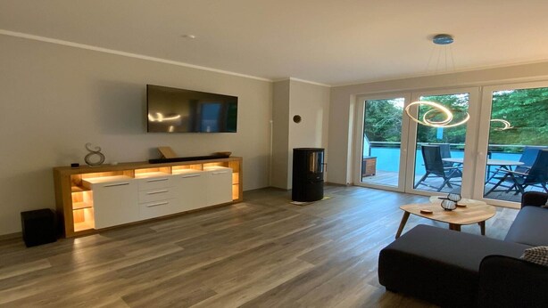 A modern living room with a wooden console table, a flat-screen TV, and a black fireplace. - Exclusives Appartement auf Fehmarn (Petersdorf)