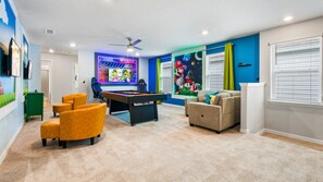 Une pièce comprenant une table de billard, deux fauteuils, un canapé, un ventilateur de plafond et une grande fresque murale.