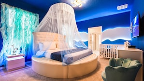 A bedroom with a round bed, a canopy, a nightstand, a dresser, a crib, and a wall with a wave design. - Last Minute Disney! Private Pool, Hot Tub, Game Room & Themed Bedrooms. Book Now! #87201 (Orlando)