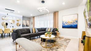 A modern living room with a sectional sofa, a round coffee table, and a dining area with chairs and a table.