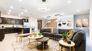 A modern living room with a sofa, two round tables, and a kitchen in the background.