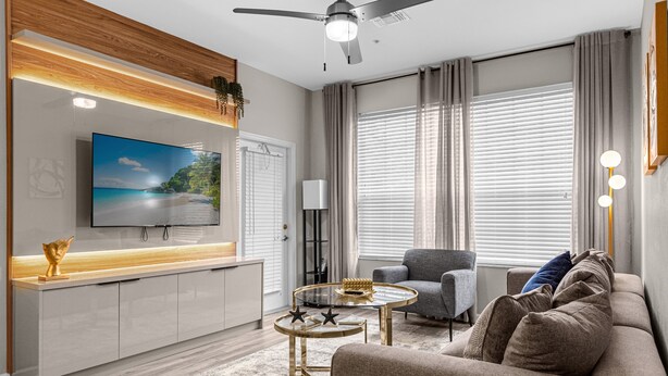 A modern living room with a flat-screen TV, a ceiling fan, a grey sofa, a round coffee table, and a wooden accent wall. - Last Minute Disney Getaway! Luxury Condo with Private Balcony. Book Now! #89639 (Orlando)