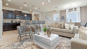 A modern living room with a sofa, chairs, a coffee table, and a kitchen in the background. - Last Minute Disney Getaway! Private Pool & Themed Bedrooms. Book Now! #90485 (Orlando)