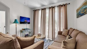 A living room with a sofa set, a television mounted on the wall, a lamp, and a window with curtains. - Last Minute Disney Getaway! Luxury Condo with Private Balcony. Book Now! #90489 (Orlando)