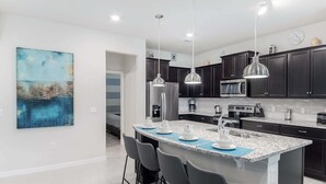A modern kitchen with dark cabinets, a granite countertop, and pendant lighting.