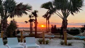 A beach scene with palm trees, lounge chairs, and a hammock.