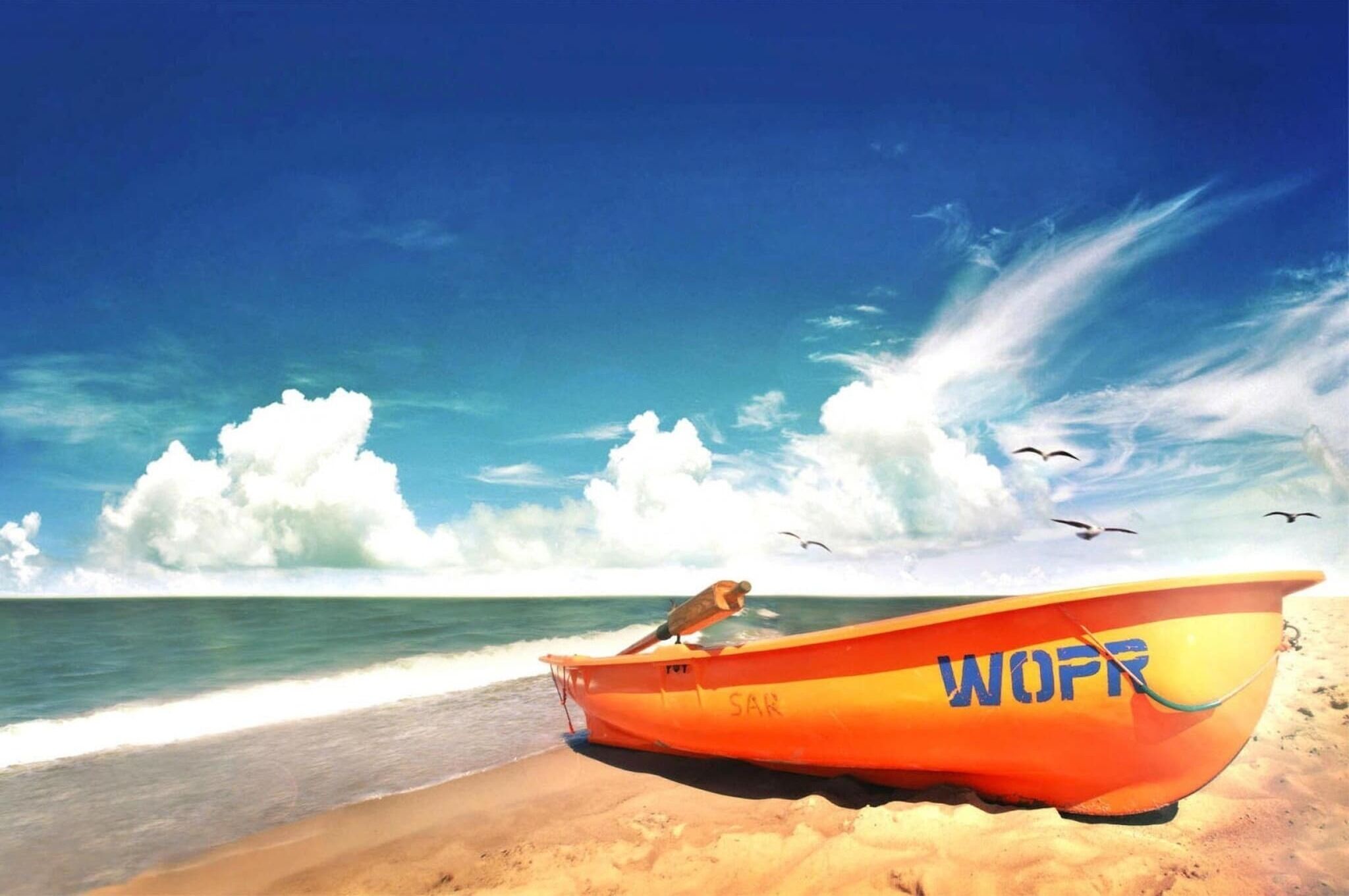 Een boot met de letters 'WOPR' op de zijkant, geparkeerd op een zandstrand met de oceaan op de achtergrond.
