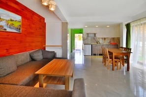 A modern living room with a wooden sofa, a wooden table, and a green door leading to a kitchen.