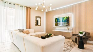 A modern living room with a sectional sofa, a flat-screen TV mounted on a wall, a decorative mirror, and a small side table with a plant. - Last Minute Disney! Private Pool, Hot Tub, Game Room & Themed Bedrooms. Book Now! #90909 (Orlando)