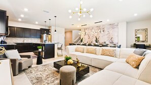 A modern living room with a large white sofa, a coffee table, and a dining area with a marble backsplash. - Last Minute Disney! Private Pool, Hot Tub, Game Room & Themed Bedrooms. Book Now! #90909 (Orlando)