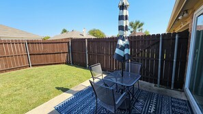 A backyard patio with a table and chairs, a striped umbrella, and a wooden fence.