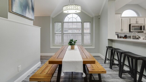 A dining area with a wooden table, benches, and a chandelier. There is a kitchen area with white cabinets and a microwave. - Lovely Lewisville great location minutes to Denton, Flower Mound, & The Colony! (Lewisville)