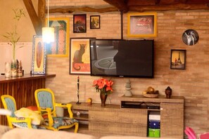 A cozy living room with a brick wall, a flat-screen TV, and a wooden entertainment unit with decorative items. - Lalabella Itagua (Ubatuba)