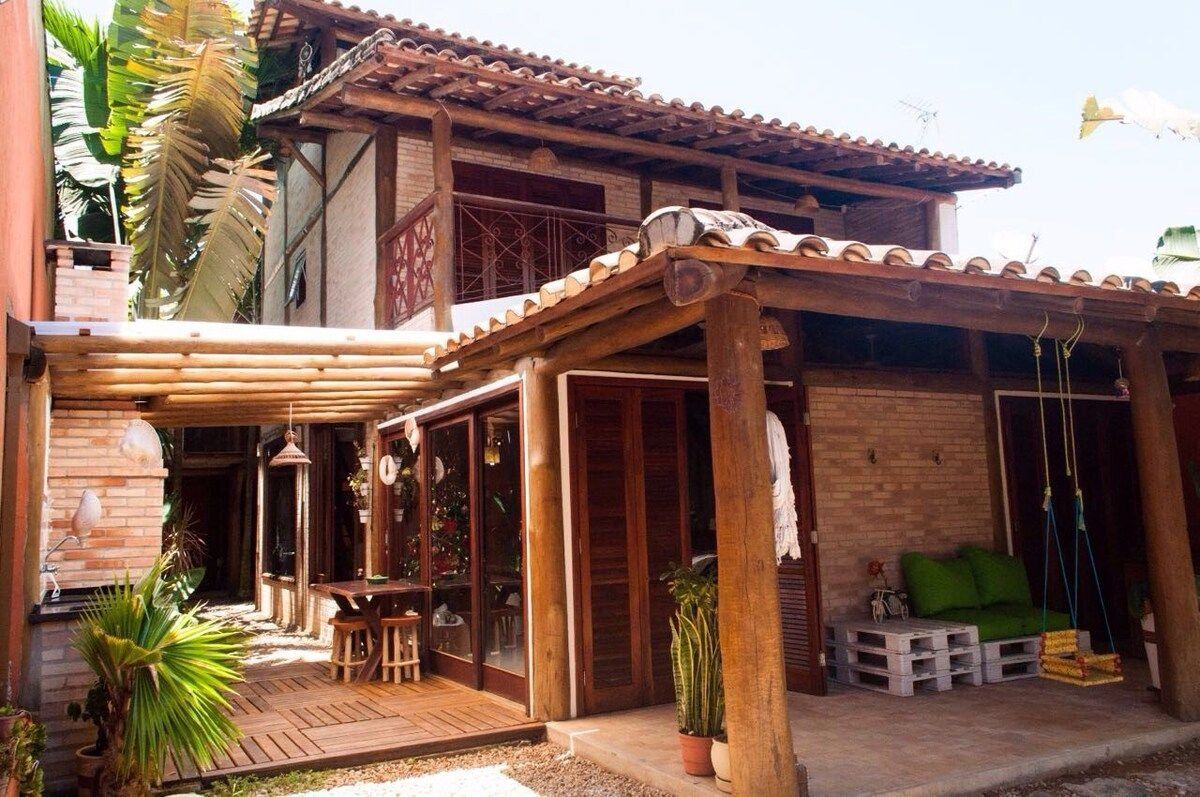 A wooden house with a patio, a swing, and a Christmas tree.