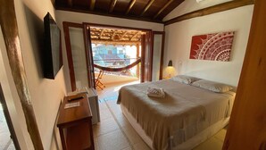 Un dormitorio con cama, mesita de noche, televisor, hamaca y vistas al exterior.