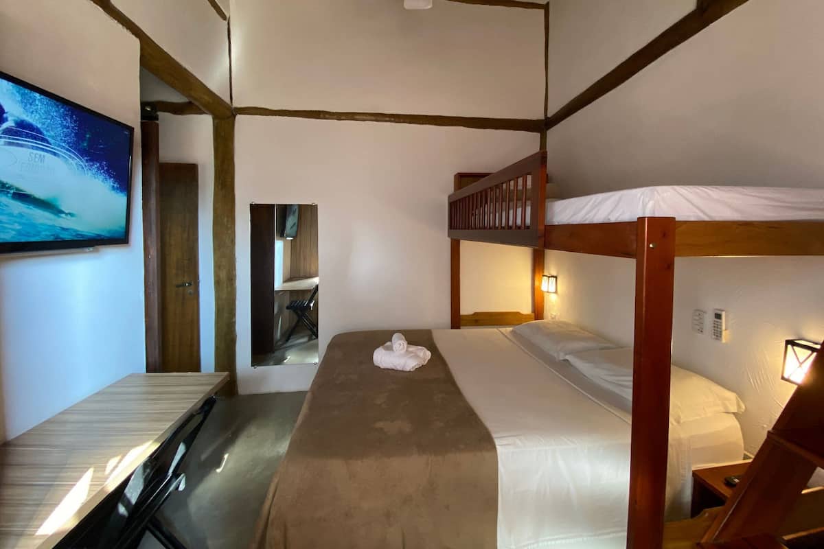 A room with a bunk bed, a desk, a chair, a television, and a ceiling fan.